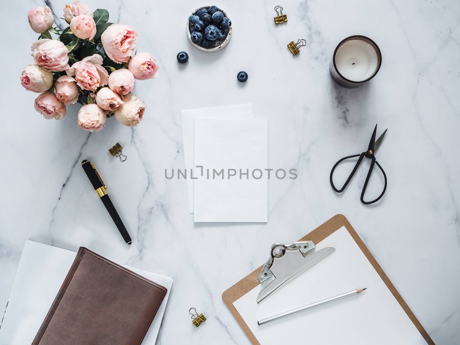 Wedding mock up. Flat lay with blank greeting card, envelope. Clipboard, flowers, scented candle on white marble. Feminine home office mock up with copy space for text or design. Flat lay