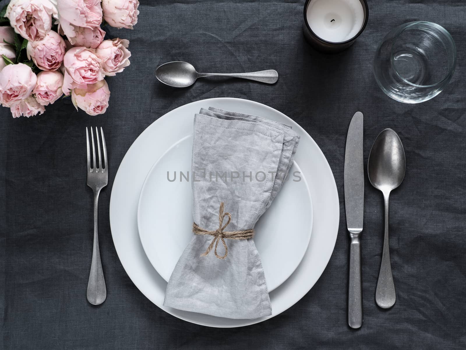 Beautiful table setting with pink spray roses and candle on gray linen tablecloth. Festive table setting for wedding dinner with gray linen napkin on plate. Holiday dinner at home, with white plates