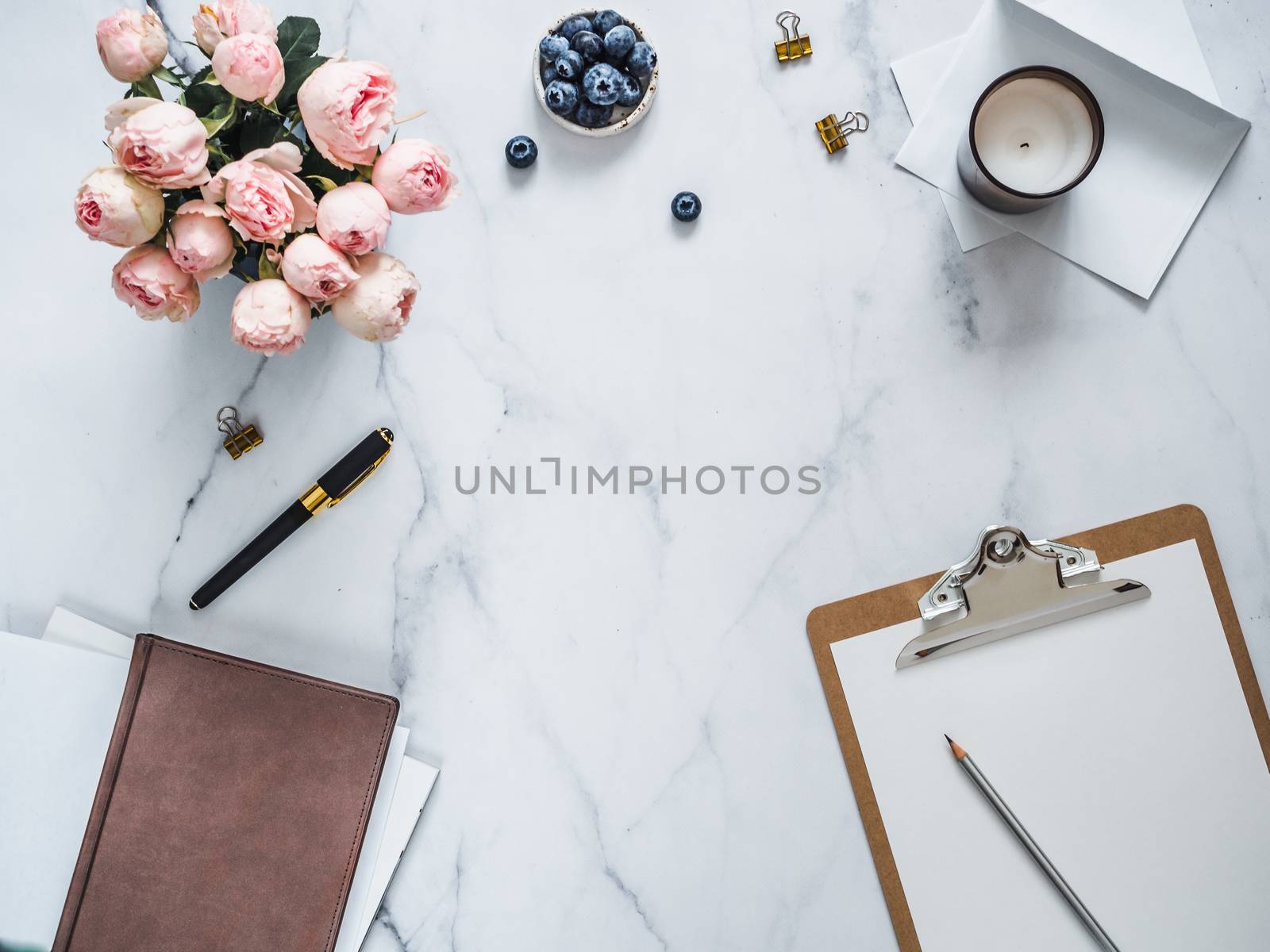 Top view of female home office with copy space in center. Clipboard, flowers, scented candle on white marble. Feminine home office mock up with copy space for text or design. Flat lay