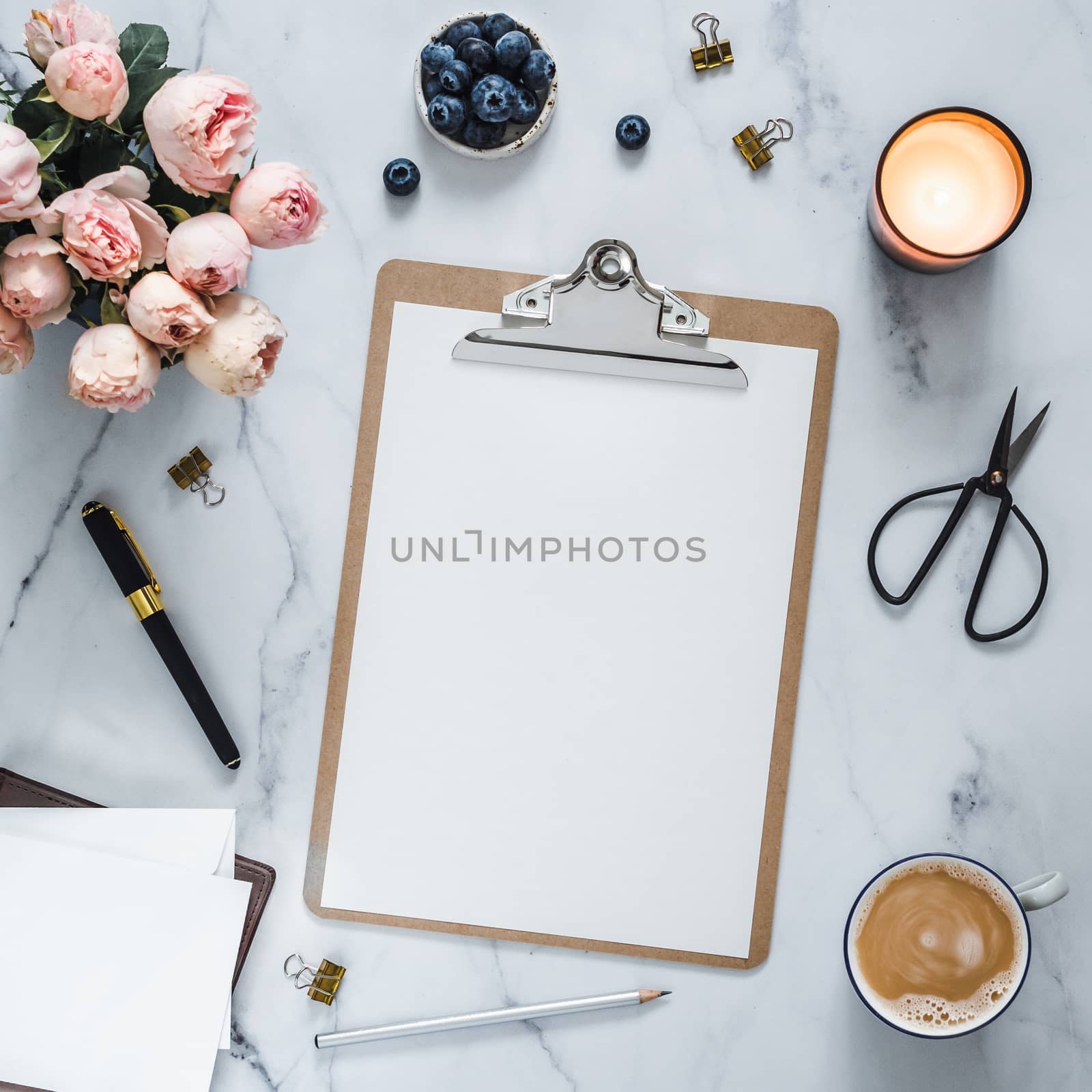 Top view of clipboard with white empty page. Clipboard, flowers, scented candle on white marble. Feminine home office mock up with blank sheet of paper A4 portrait format,copy space for text. Flat lay