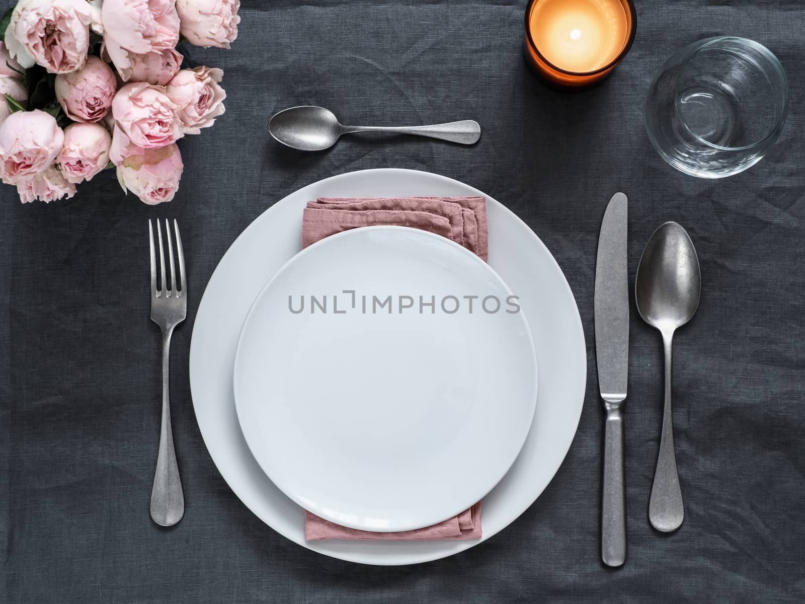 Beautiful table setting on gray linen tablecloth. Festive table setting for wedding dinner with pink spray roses and scented cabdle. Holiday dinner with white plates. Dinner, utensil. Copy space