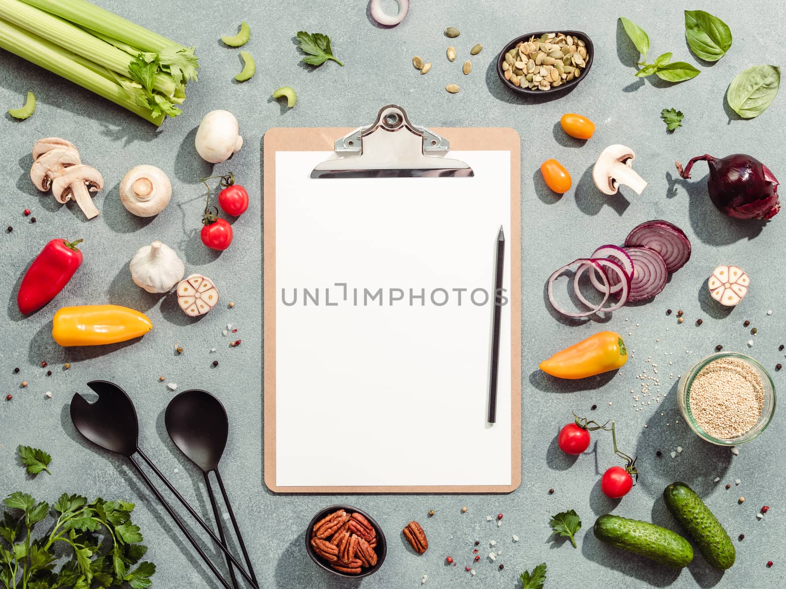 Food ingredients, salad serving utensils and clipboard with white paper sheet. Various of vegetarian cooking ingredients on gray background.Recipe book concept.Copy space for text.Top view or flat lay