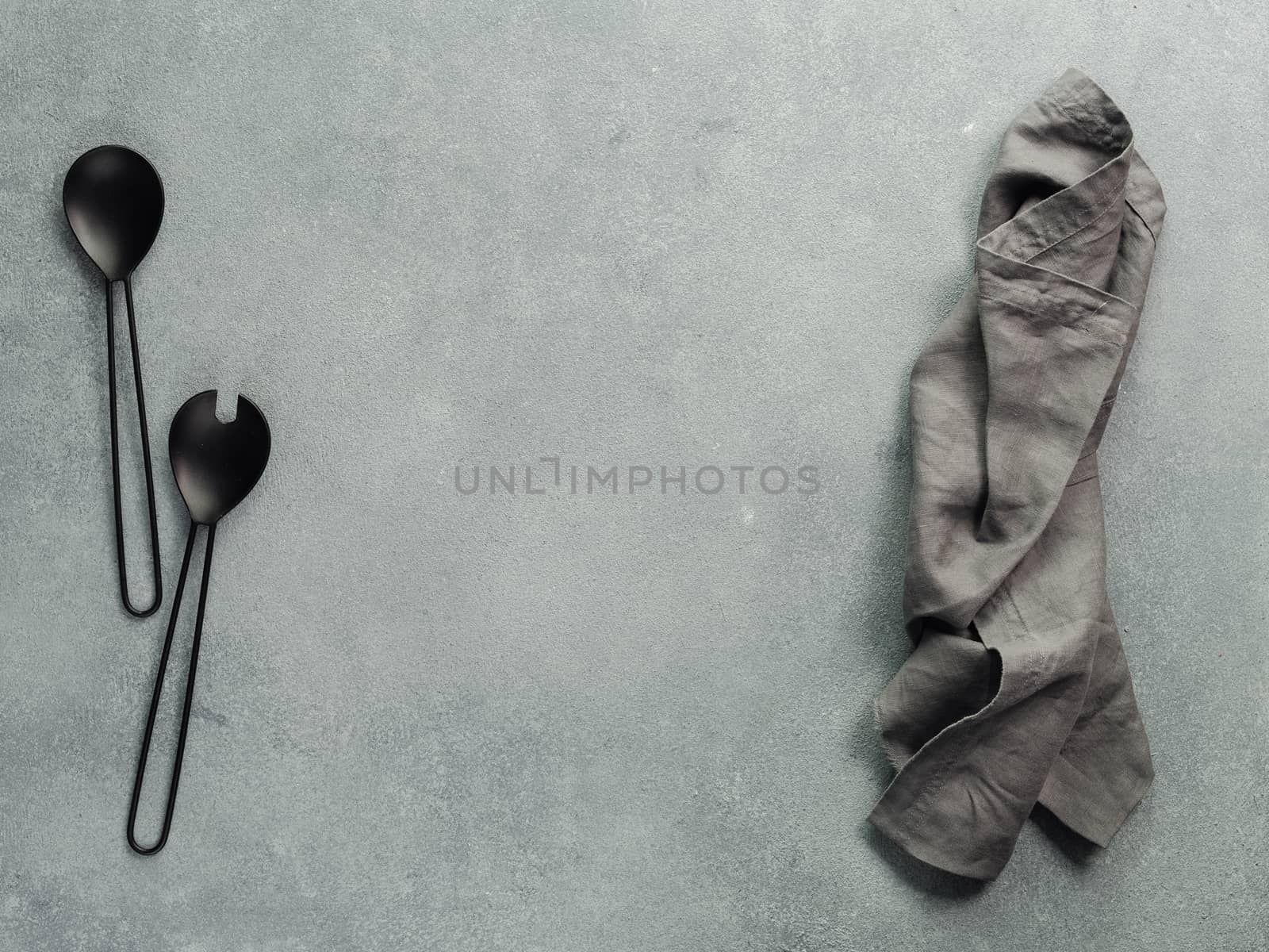 Salad serving utensils, folded linen napkin or towel with copy space for design. Salad utensils on gray stone background. Recipe, diet, salad,cooking concept. Copy space for text. Top view or flat lay