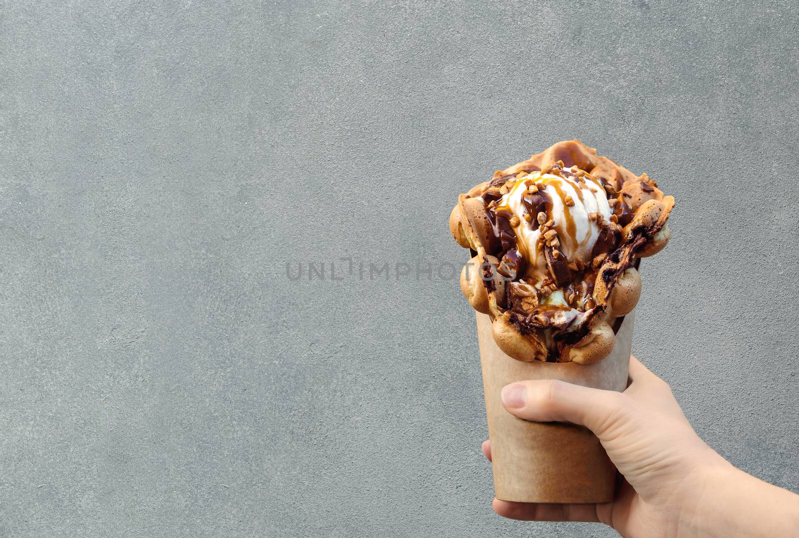 Hong Kong waffles in female hand on brick wall background. Delicious bubble waffle with ice cream and caramel syrup in woman hand. Trendy food. Copy space for text