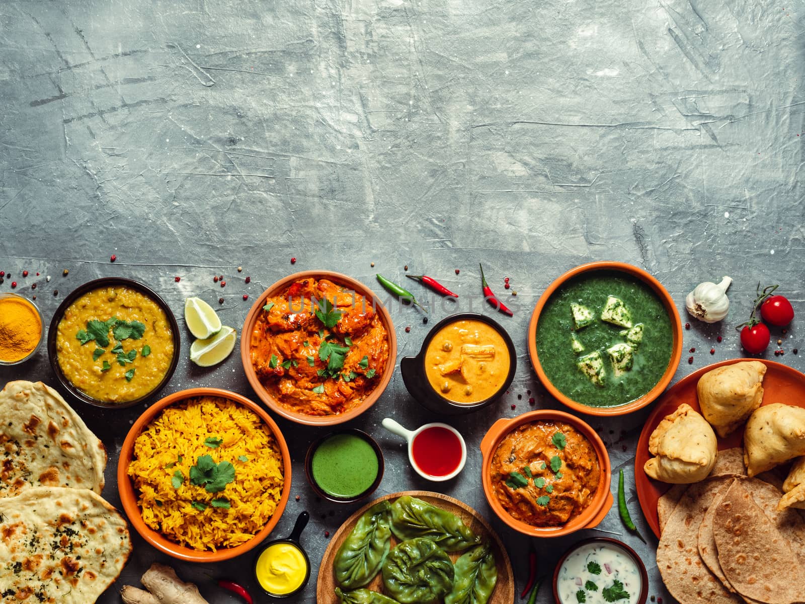 Indian cuisine dishes: tikka masala, dal, paneer, samosa, chapati, chutney, spices. Indian food on gray background. Assortment indian meal with copy space for text. Top view or flat lay.