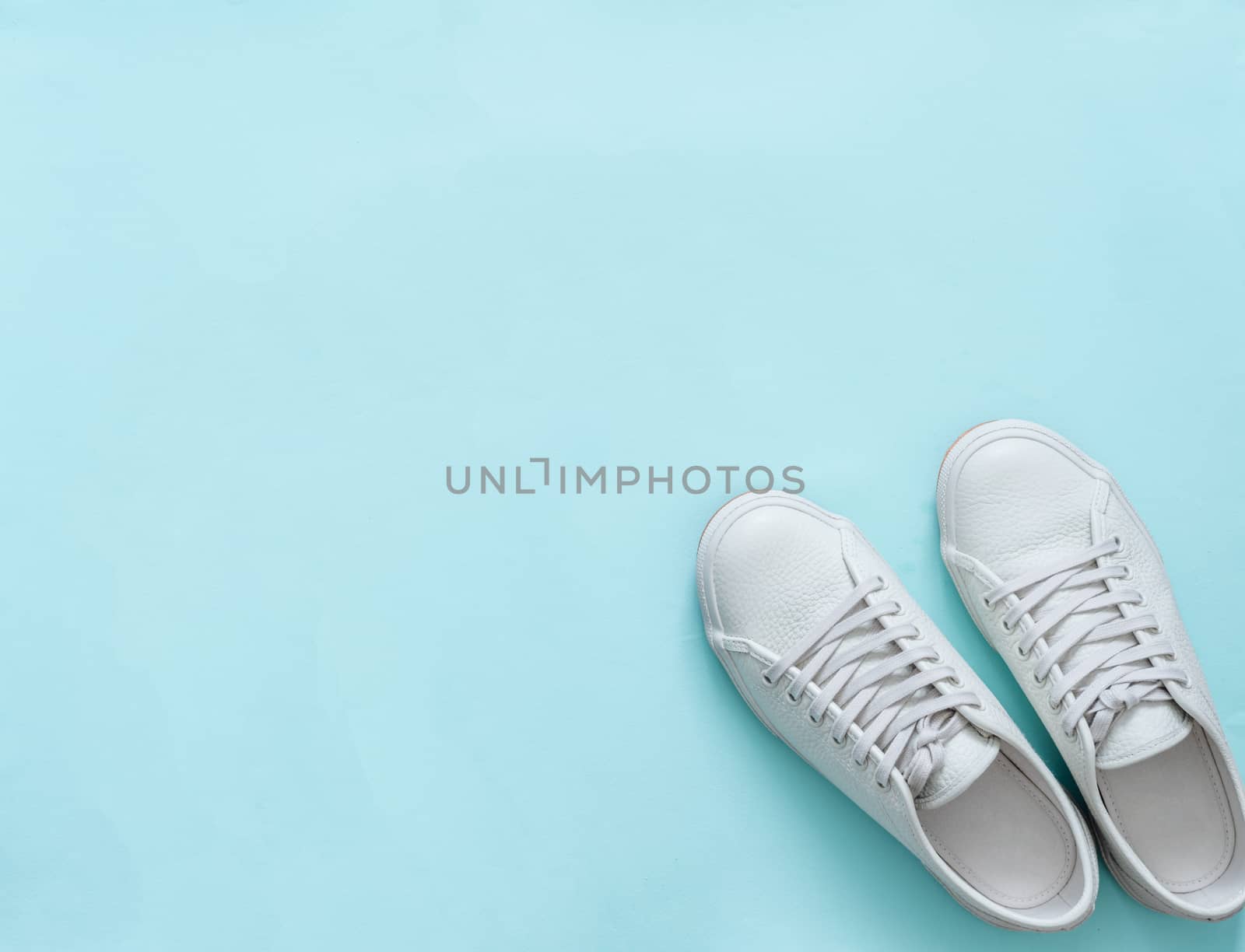 White leather sneakers on blue background. Pair of fashion trendy white sport shoes or sneakers with copy space for text or design. Overhead shot of new white sneakers. Top view or flat lay.