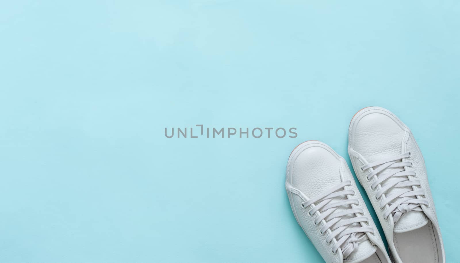 White leather sneakers on blue background. Pair of fashion trendy white sport shoes or sneakers with copy space for text or design. Overhead shot of new white sneakers. Top view or flat lay. Banner