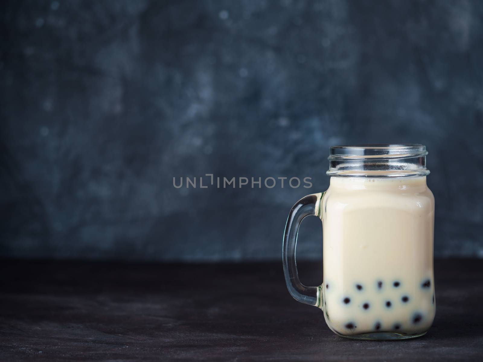Homemade Milk Bubble Tea with Tapioca Pearls balls. Popular Taiwan bubble tea in glass mason jar with copy space for text. Bubble tea on dark background.