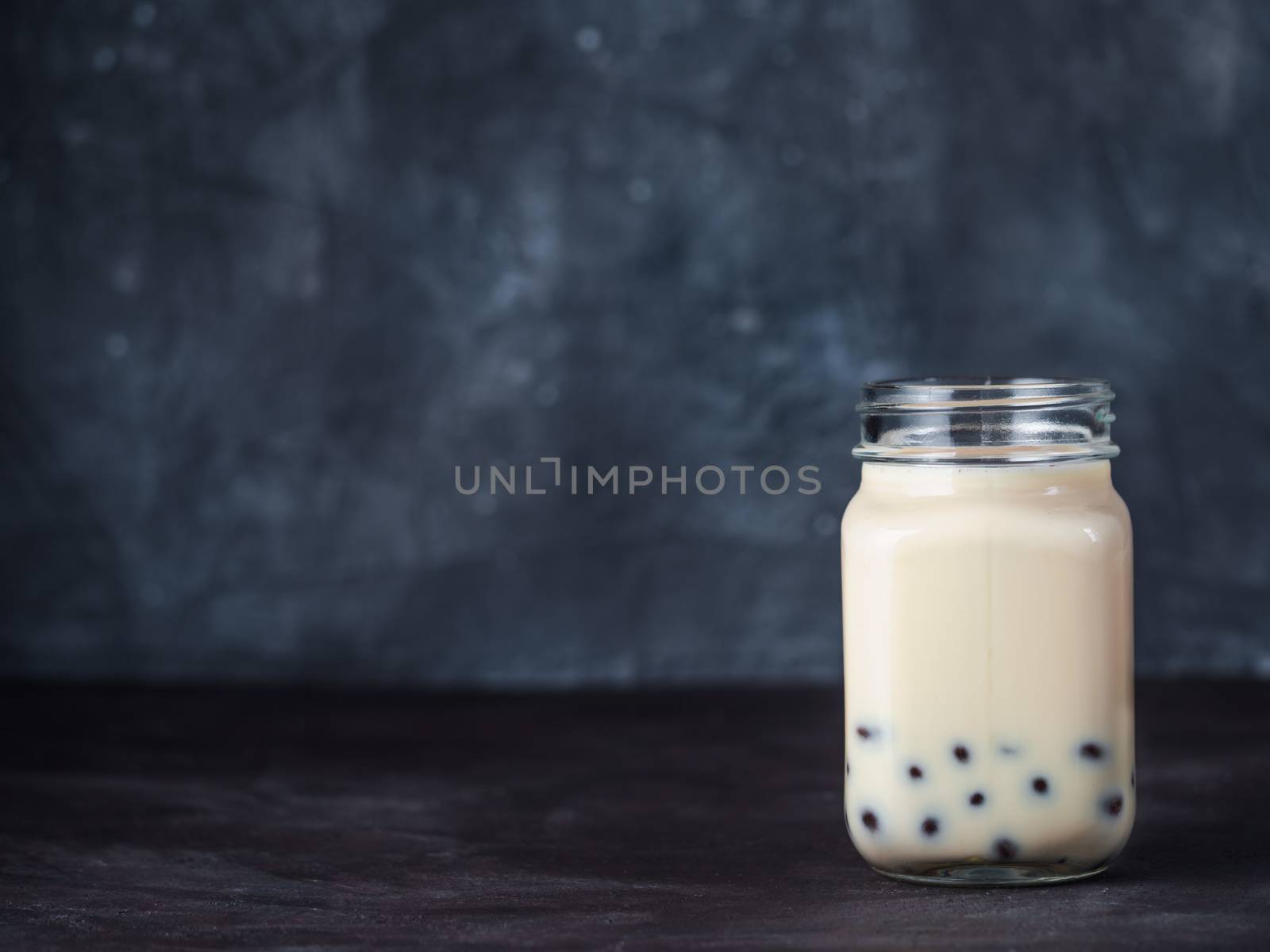 Homemade Milk Bubble Tea with Tapioca Pearls balls. Popular Taiwan bubble tea in glass mason jar with copy space for text. Bubble tea on dark background.