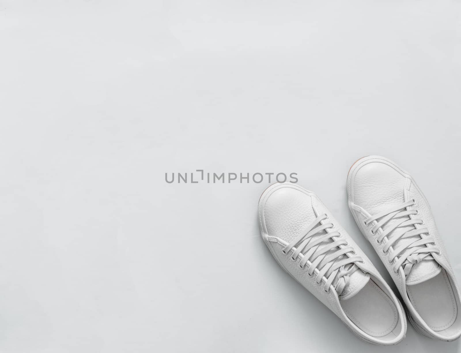 White leather sneakers on white background. Pair of fashion trendy white sport shoes or sneakers with copy space for text or design. Overhead shot of new white sneakers,monochrome.Top view or flat lay