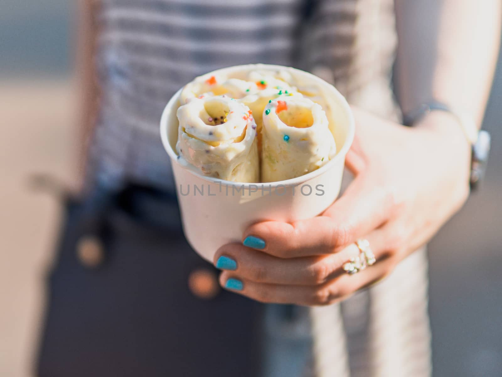 Rolled ice cream in cone cup in woman hands. Woman in striped dress holds cone cup with thai style kiwi banana rolled ice cream.