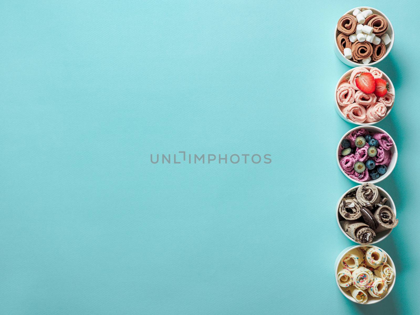 Rolled ice creams in paper cone cups on blue background. Different iced rolls, top view or flat lay. Thai style rolled ice cream with copy space for text or design