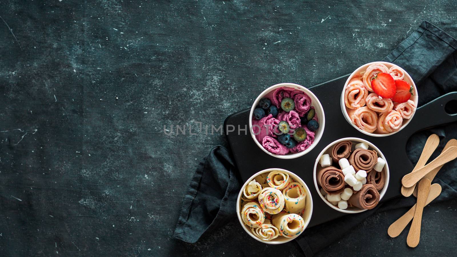 Rolled ice cream in cone cups on dark background. Different iced rolls top view or flat lay. Thai style rolled ice cream with copy space in center for text or design. Banner