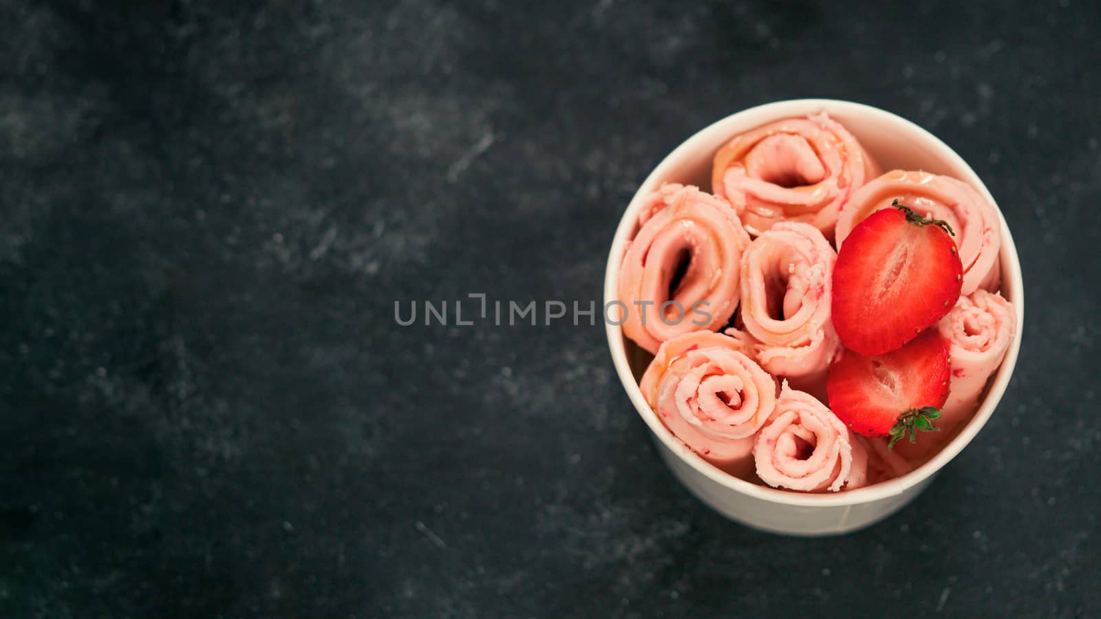 Rolled ice cream with strawberry in cone cup on dark background. Strawberry iced rolls top view or flat lay. Thai style rolled ice cream with copy space for text or design. Banner
