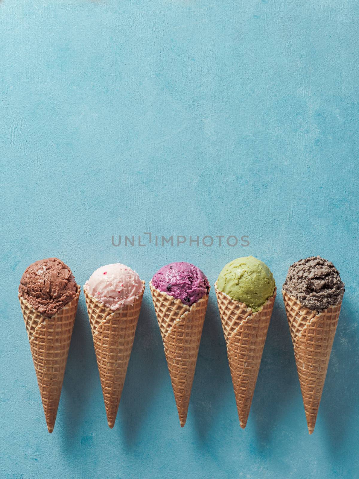 Various ice cream scoops in cones with copy space. Colorful ice cream in cones chocolate, strawberry, blueberry, pistachio or matcha, biscuits chocolate sandwich cookies on blue background. Top view