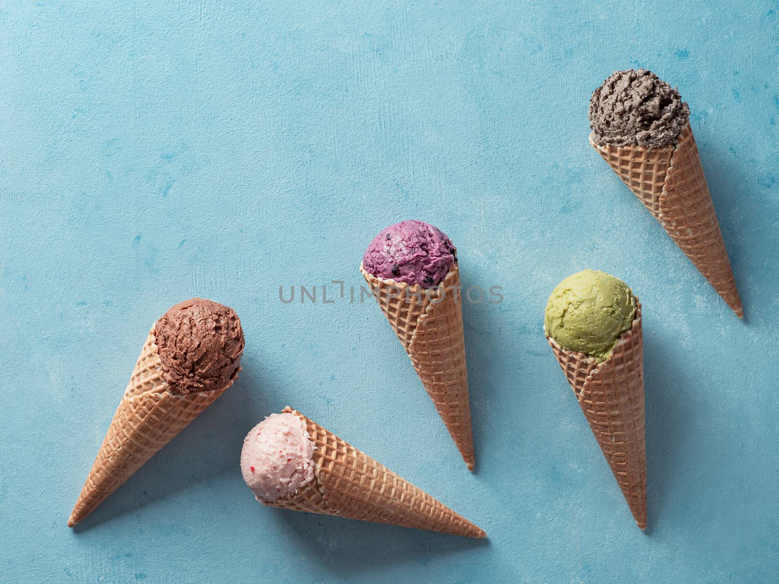 Various ice cream scoops in cones with copy space. Colorful ice cream in cones chocolate, strawberry, blueberry, pistachio or matcha, biscuits chocolate sandwich cookies on blue background. Top view