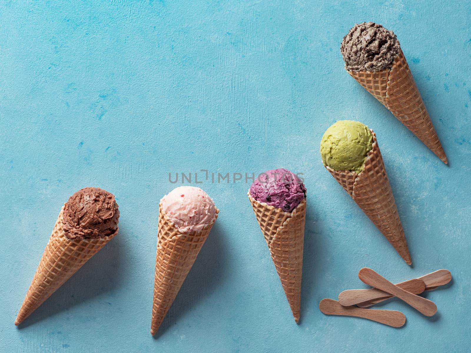 Various ice cream scoops in cones with copy space. Colorful ice cream in cones chocolate, strawberry, blueberry, pistachio or matcha, biscuits chocolate sandwich cookies on blue background. Top view