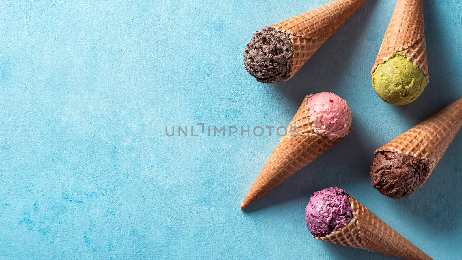 Various ice cream scoops in cones with copy space. Colorful ice cream in cones chocolate, strawberry, blueberry, pistachio or matcha, biscuits chocolate sandwich cookies on blue background. Top view