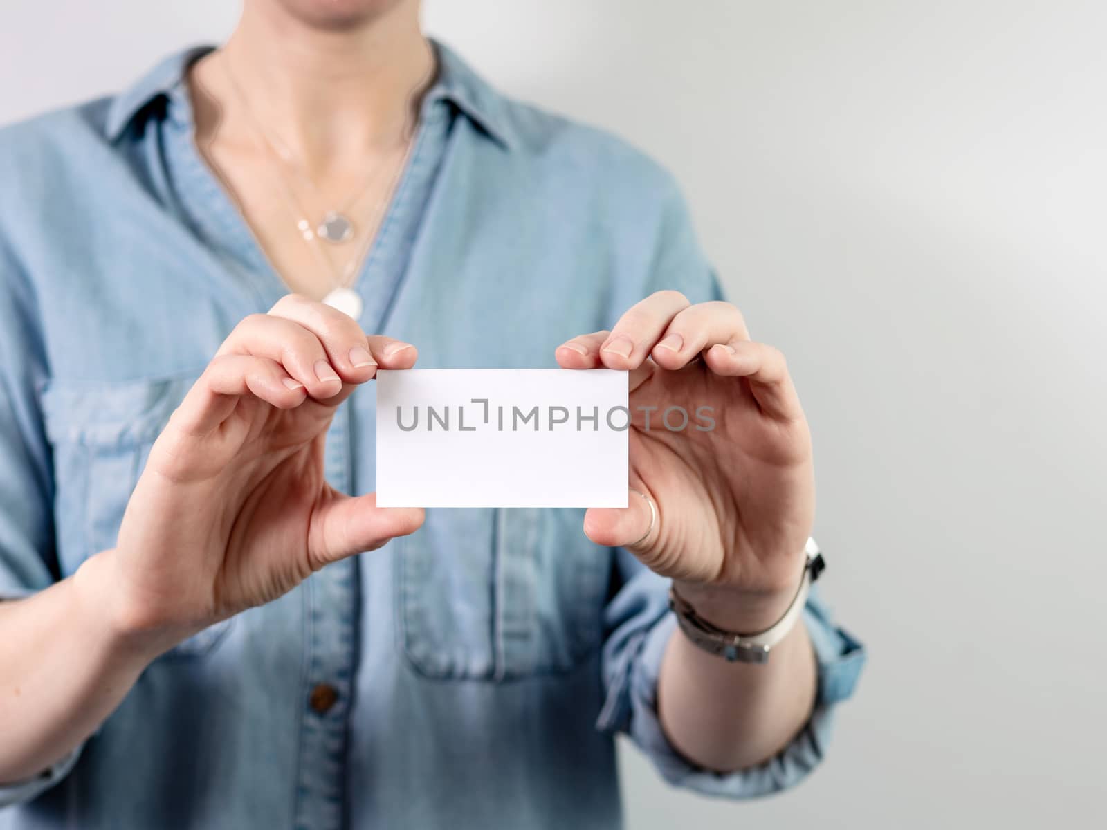 Female hands hold blank white card mockup. Plain call-card mock up template holding woman arm. Caucasian woman in casual blue denim shirt with business card display front. Check offset card design