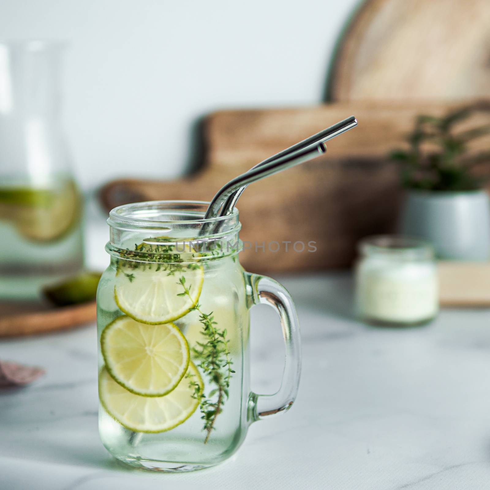 Cold drink in mason jar with metal straws on kitchen table. Lemonade or detox water with lime and thyme in glass jar wit metal straw indoor. Recyclable straws, zero waste concept