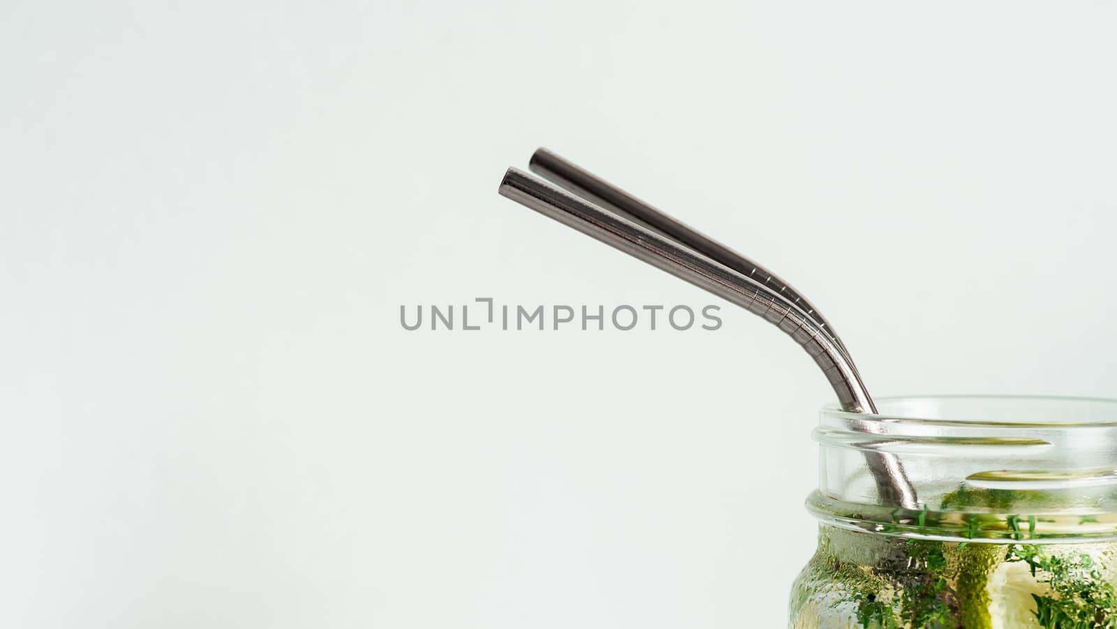 Cold drink in mason jar with metal straw on white background. Lemonade or detox water with lime and thyme in glass jar with copy space for text or design. Recyclable straws, zero waste concept. Banner