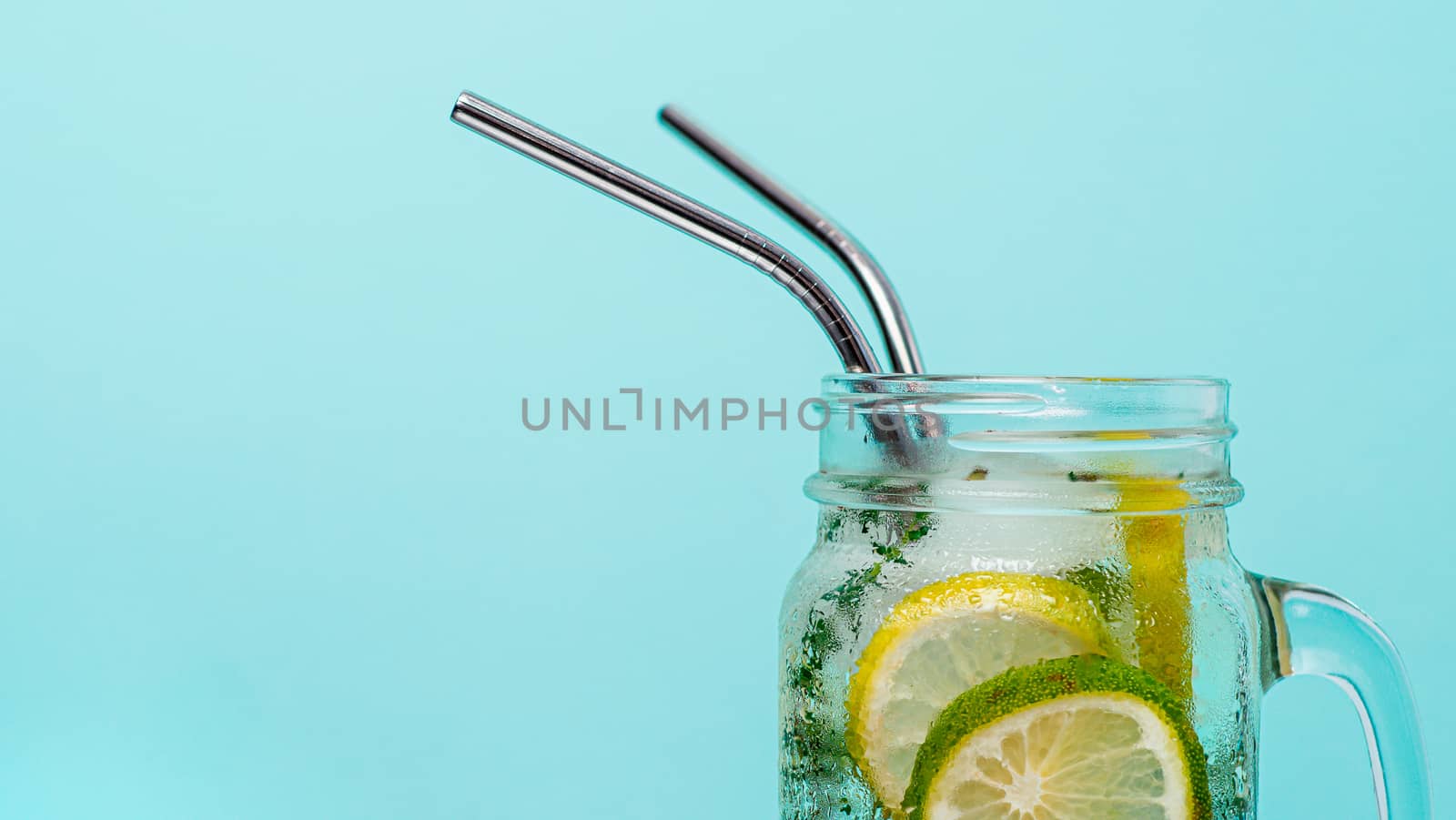 Cold drink in mason jar with metal straw on blue background. Lemonade or detox water with lime and thyme in glass jar with copy space for text or design. Recyclable straws, zero waste concept. Banner.