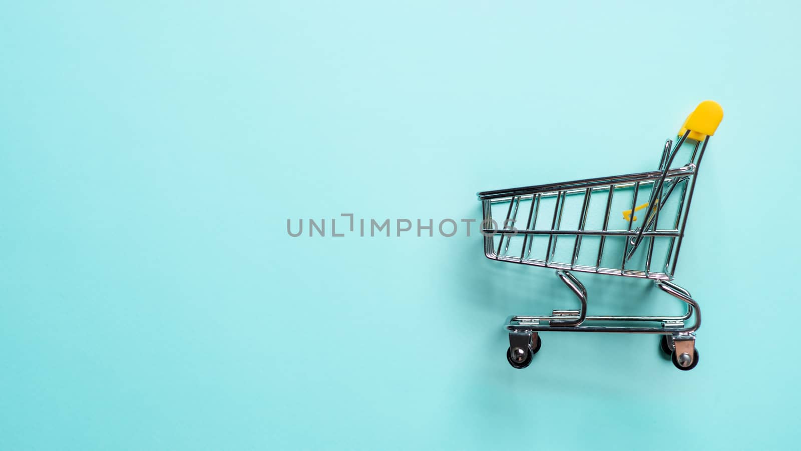 Shopping cart on blue background. Top view or flat lay. Shop trolley at supermarket as sale, discount, shopaholism concept with copy space for text or design. Consumer society trend.