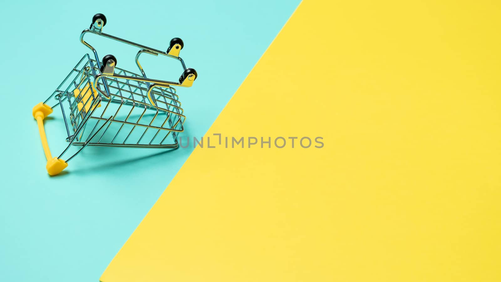 Empty inverted shopping cart on blue and yellow background. Inverted toy trolley on bright colorful background, copy space for text or design.