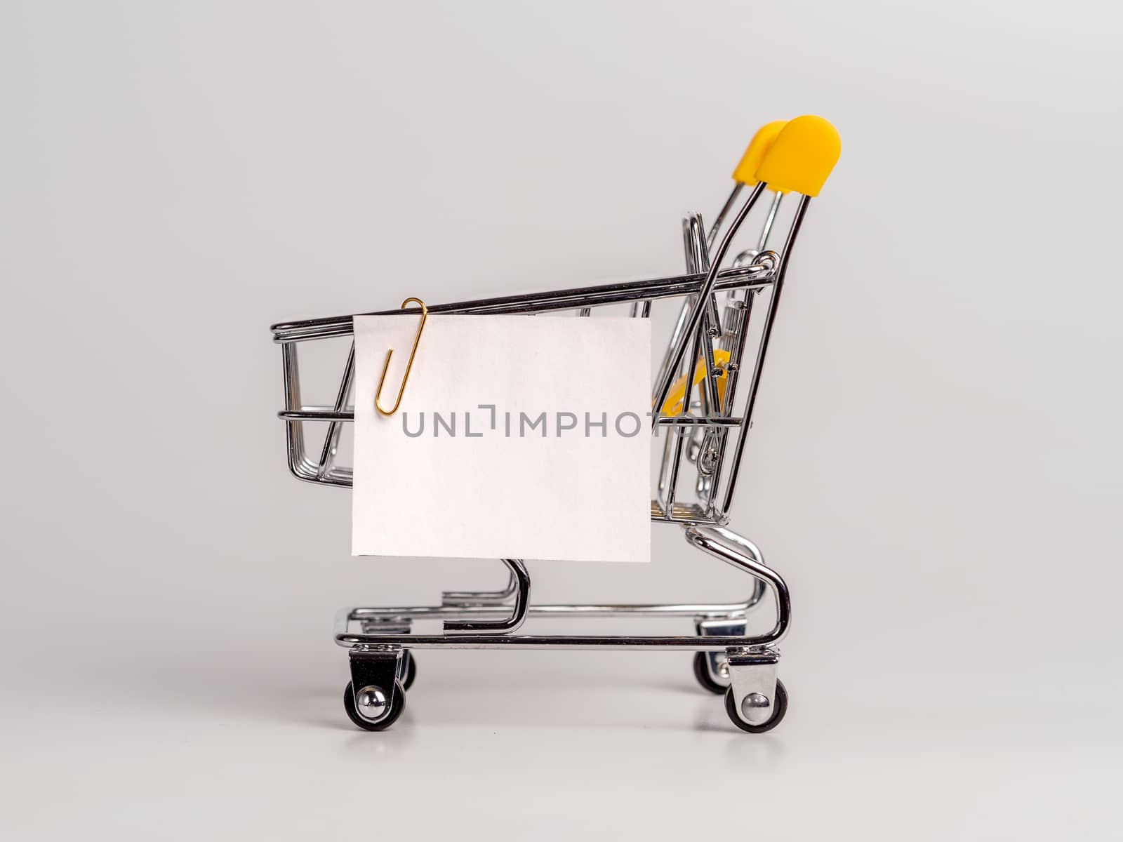 Shopping cart and white paper note list isolated on white background. Shopping concept on light monochrome background. Empty white paper note over shopping cart. Copy space for text or design.