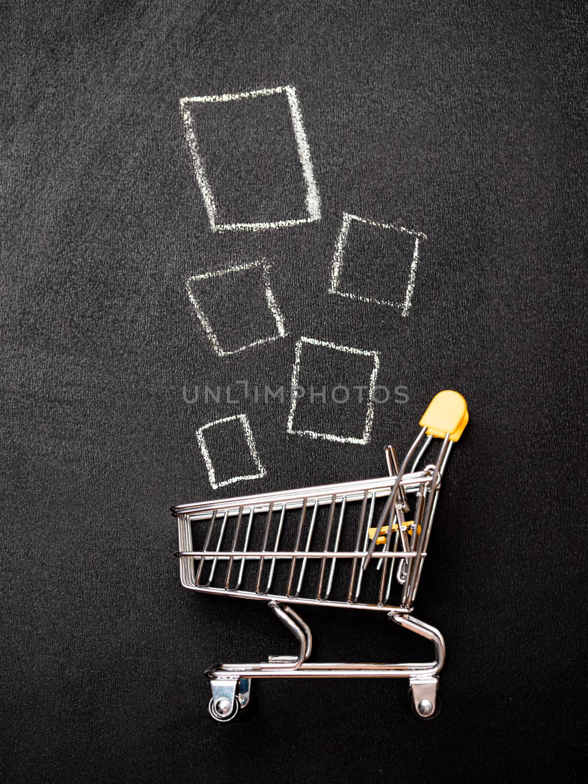 Shopping cart and products on chalkboard. Shop trolley at supermarket as sale, discount, shopaholism concept. Top view or flat lay. Vertical