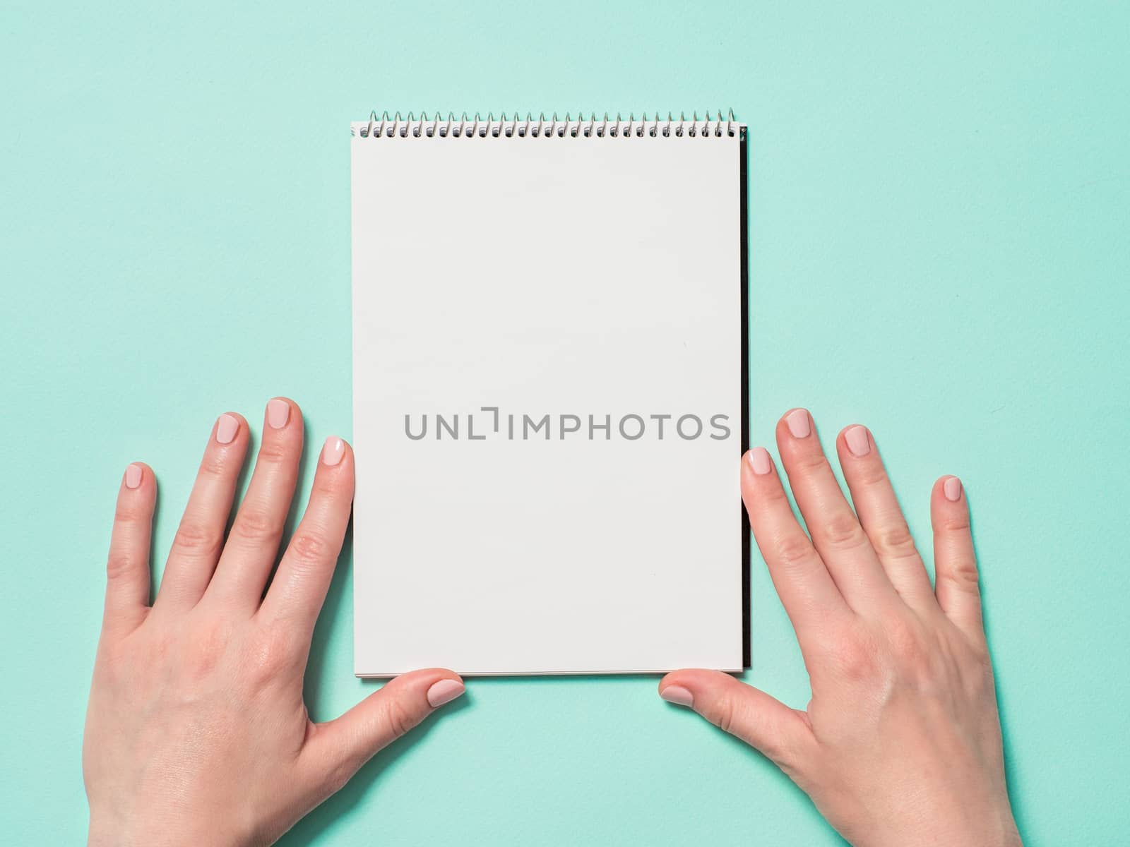 Blank paper notebook and female hands. Empty paper sketchbook and woman hands on blue background. Top view or flat lay. Copy space for text or design.