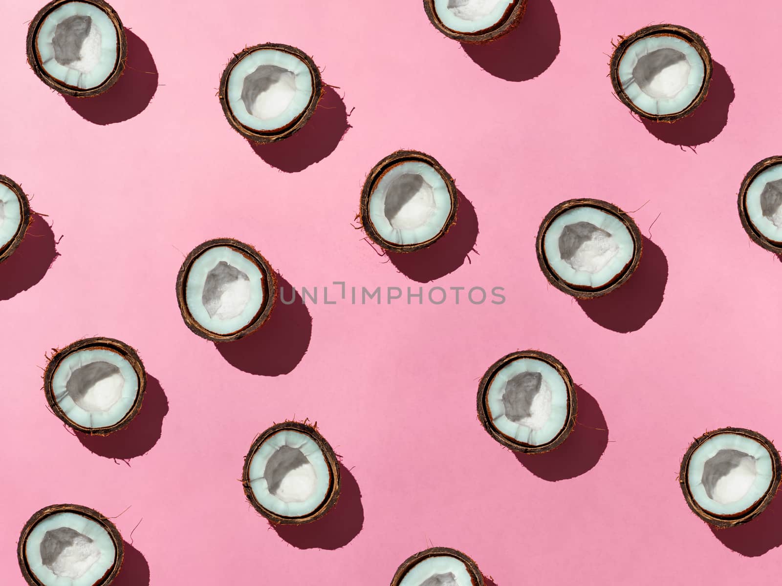 Creative layout of coconuts half on pink background. Tropical pattern, top view or flat lay. Hard light pop art minimal summer background.