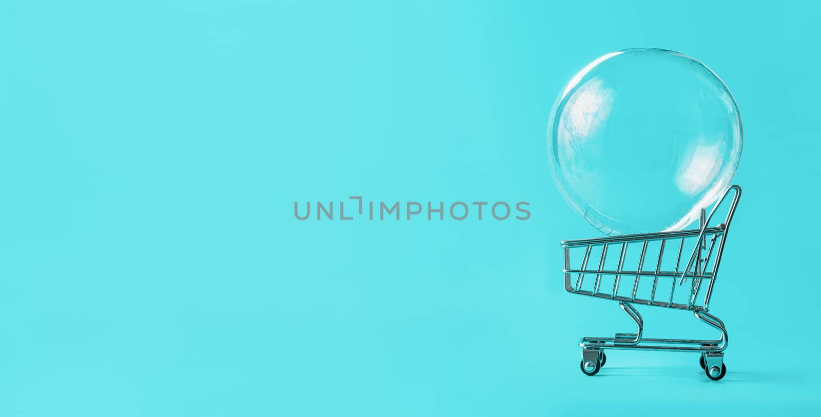 Shopping cart with soap bubble on bright blue background. Ephemeral happiness from shopping, shopaholism, consumerism concept. Shopping concept, minimalist creative layout, copy space for text. Banner
