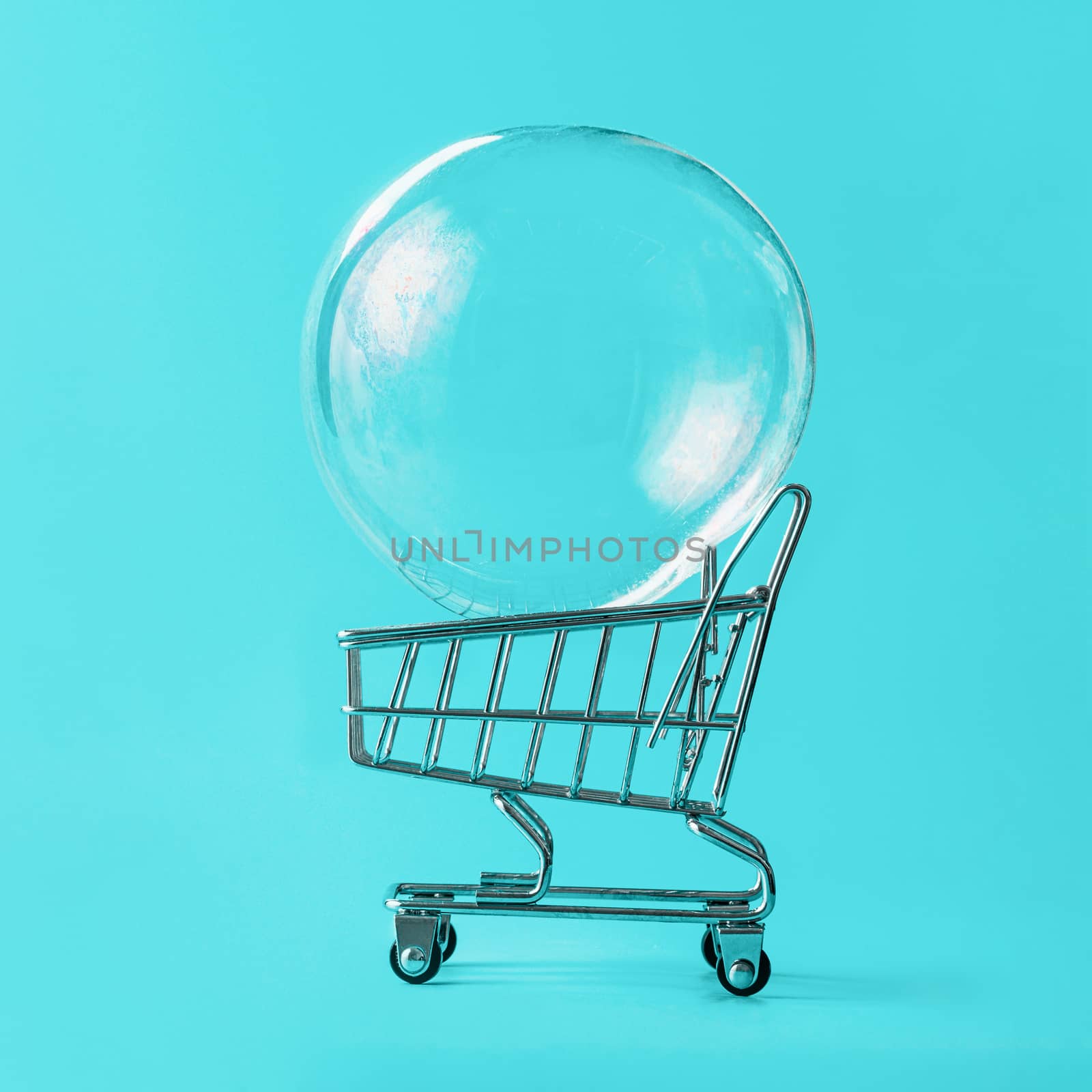 Shopping cart with soap bubble on bright blue background. Ephemeral happiness from shopping, shopaholism, consumerism concept. Shopping concept, minimalist creative layout