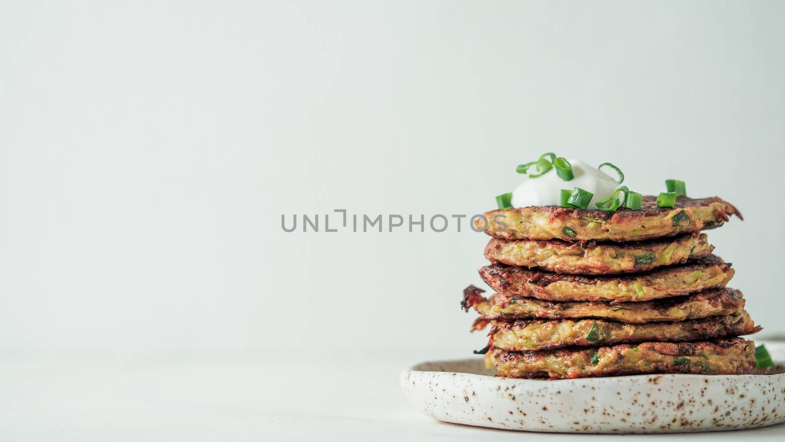 Gluten free zucchini fritters in stack on white background. Zucchini pancakes or fritters with green onion and parmesan cheese, served sour cream or greek yogurt Banner. Copy space