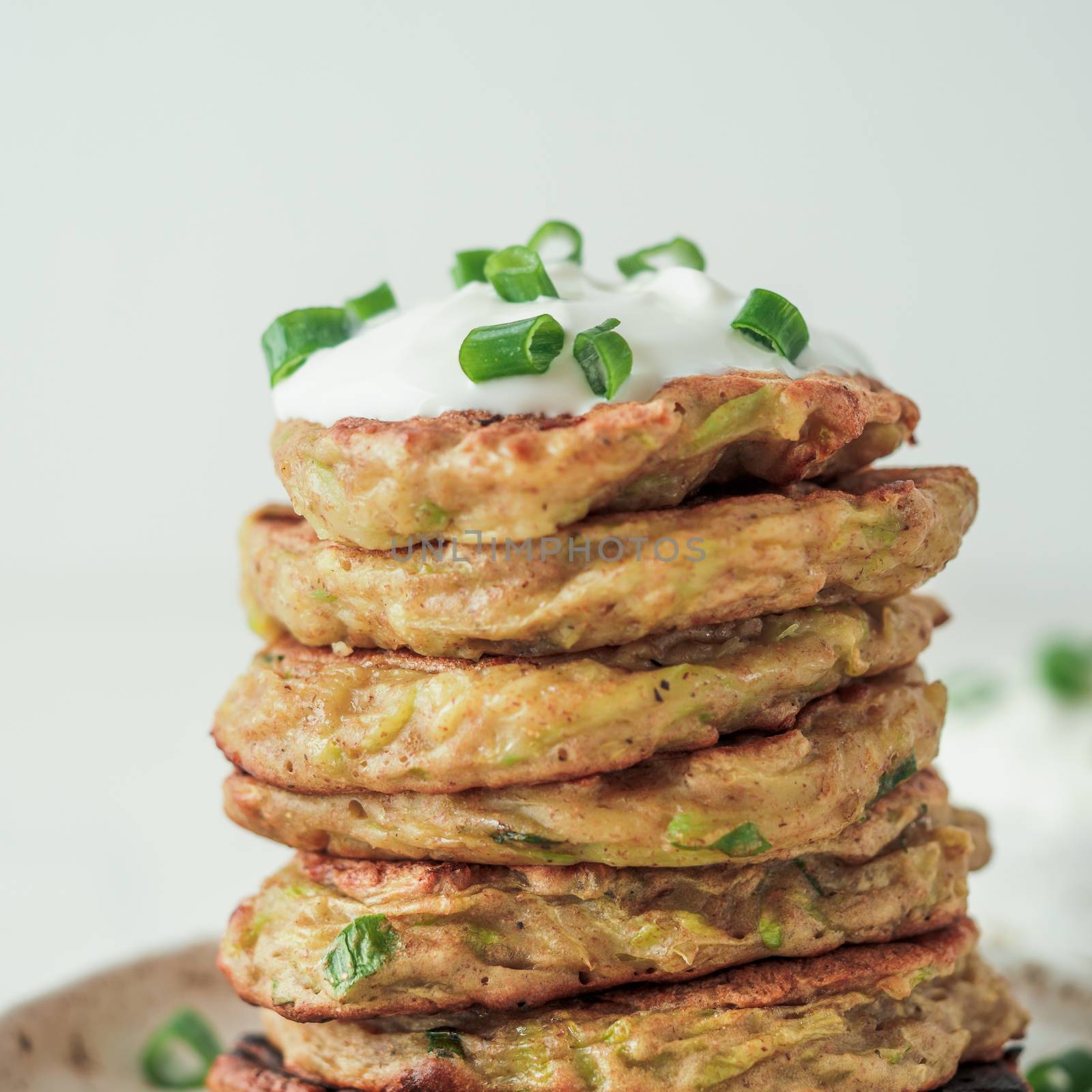 Zucchini fritters. Gluten free zucchini fritters in stack on white background. Vegetable zucchini pancakes or fritters with green onion and parmesan cheese, served sour cream or greek yogurt