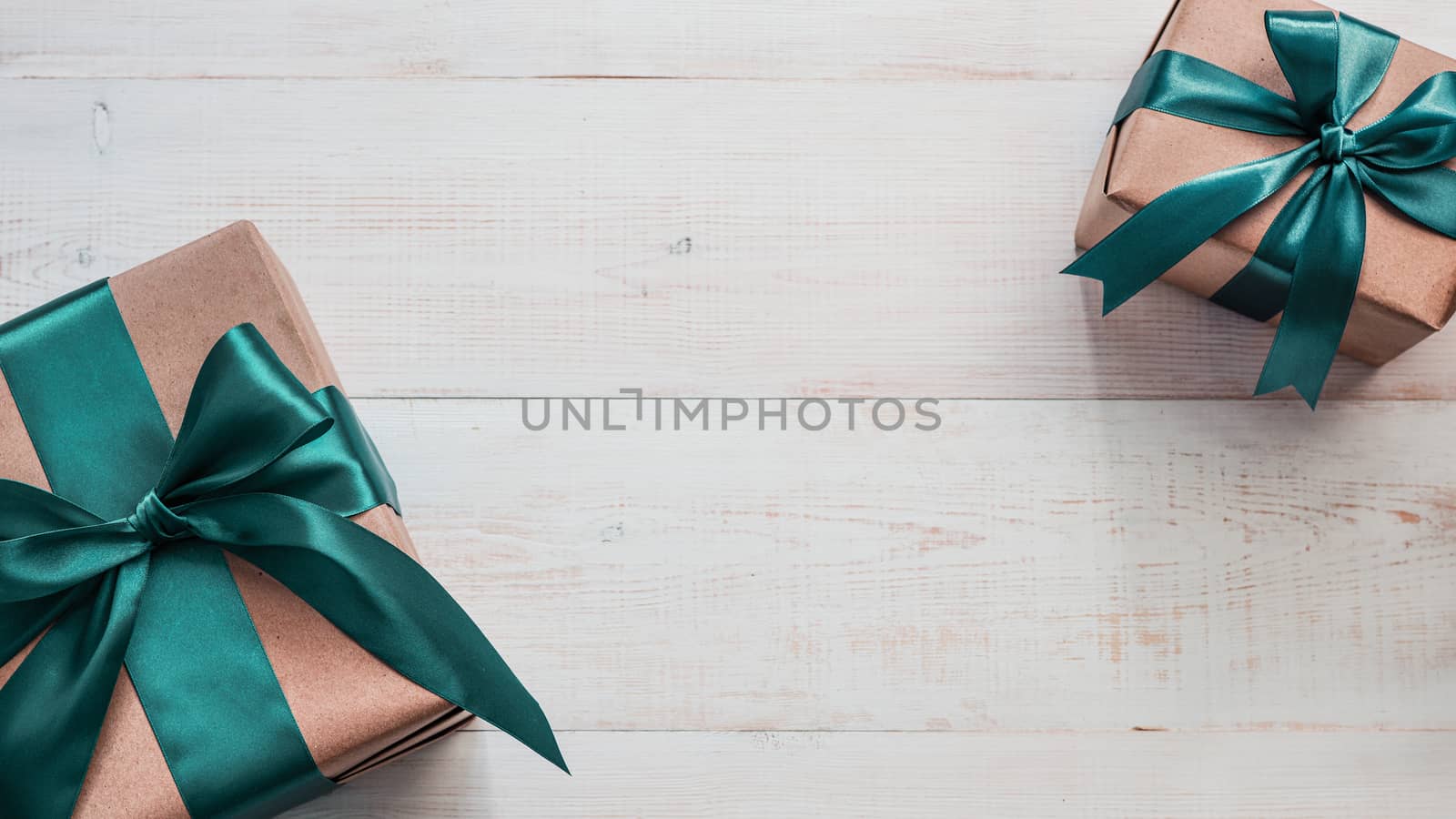 Two gift boxes in craft wrapping paper and green satin ribbon on white wooden table, copy space in center. Beautiful Christmas, New Year or Birthday presents, flat lay or top view. Banner