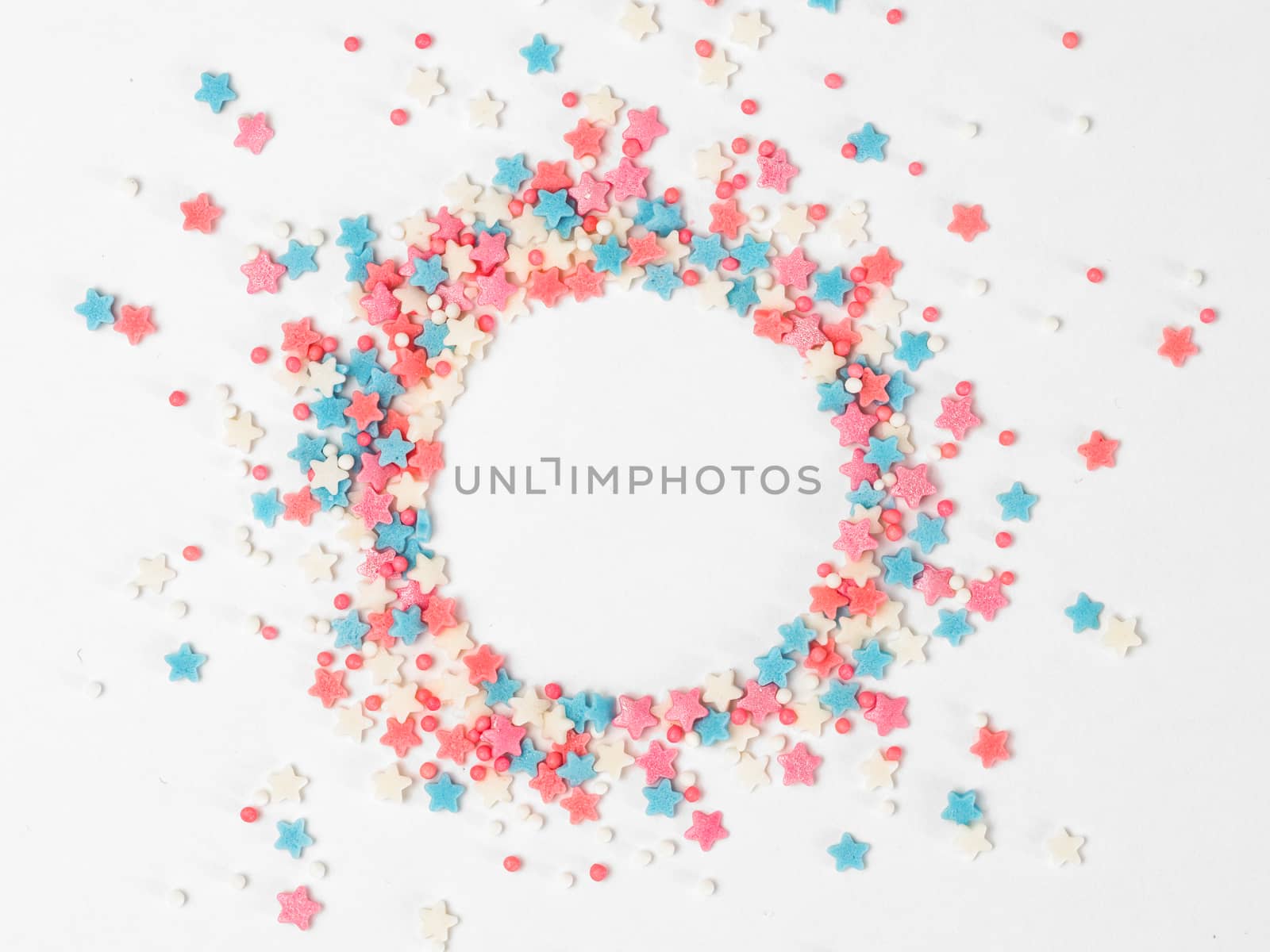 Festive border frame of colorful pastel sprinkles on white background with copy space in center. Sugar sprinkle dots and stars in round shape, decoration for cake and bakery. Top view or flat lay