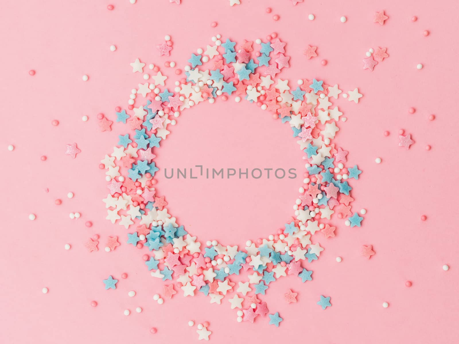 Festive border frame of colorful pastel sprinkles on pink background with copy space in center. Sugar sprinkle dots and stars in round shape, decoration for cake and bakery. Top view or flat lay