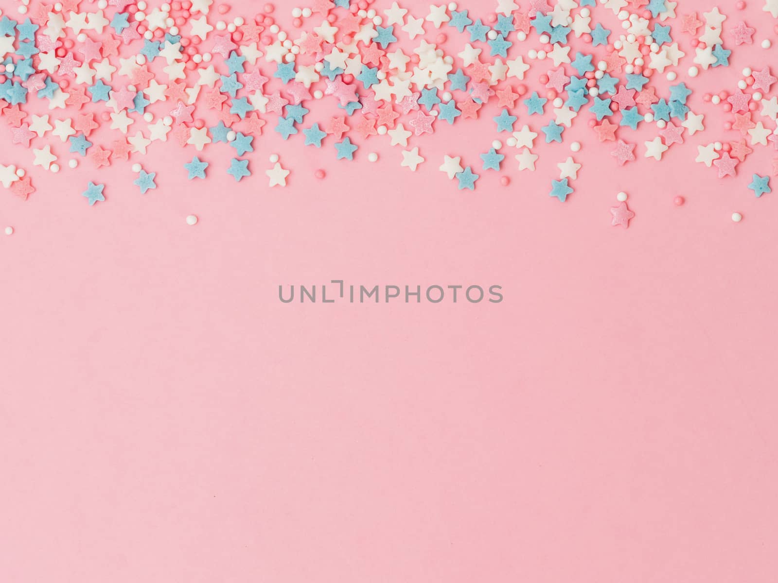 Festive border frame of colorful pastel sprinkles on pink background, copy space top. Sugar sprinkle dots and stars, decoration for cake and bakery. Top view or flat lay