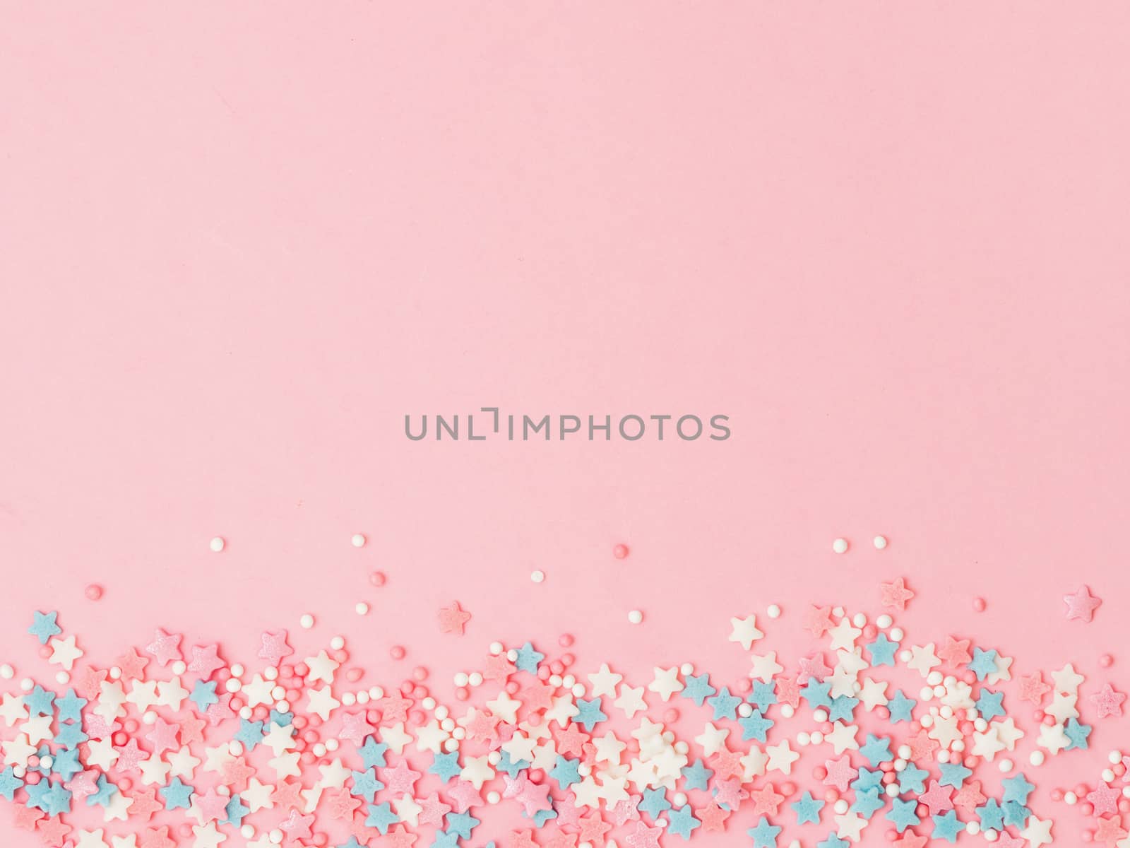Festive border frame of colorful pastel sprinkles on pink background, copy space top. Sugar sprinkle dots and stars, decoration for cake and bakery. Top view or flat lay