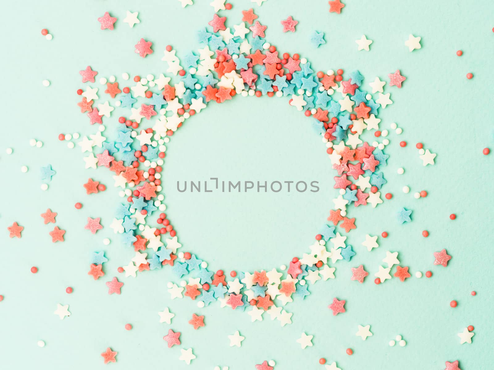 Festive border frame of colorful pastel sprinkles on blue background with copy space in center. Sugar sprinkle dots and stars in round shape, decoration for cake and bakery. Top view or flat lay
