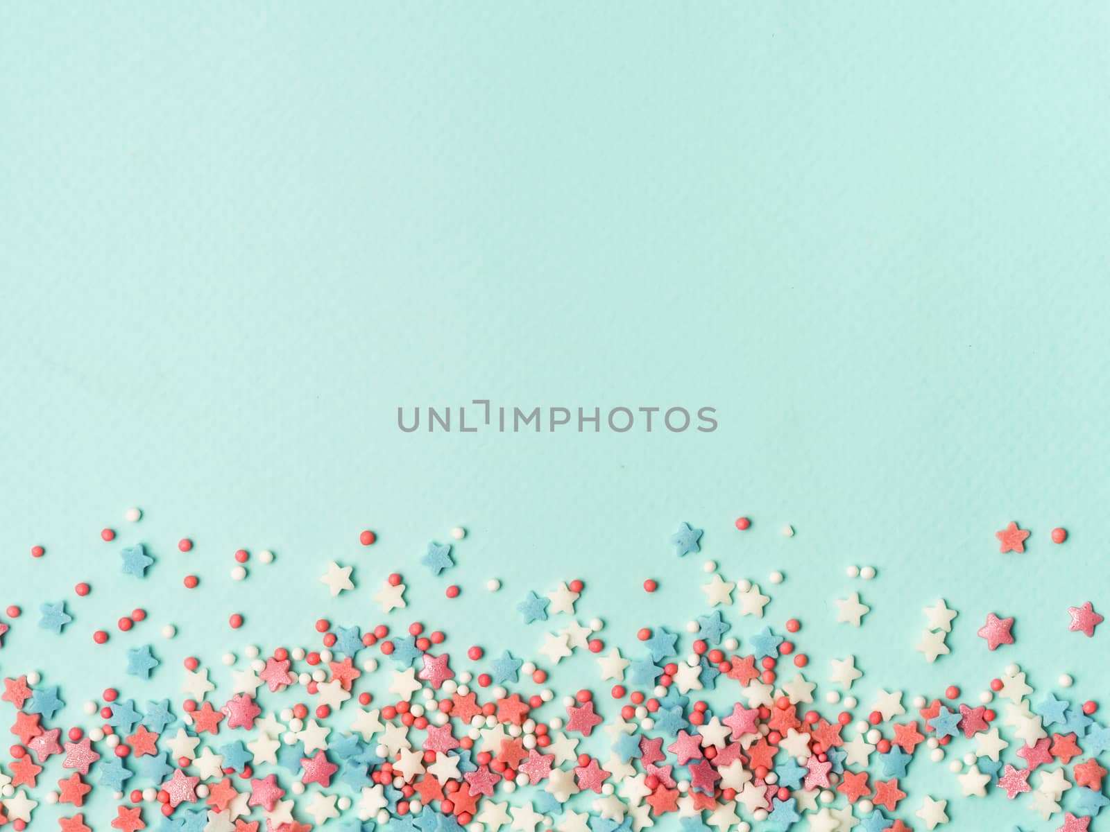 Festive border frame of colorful pastel sprinkles on blue background, copy space top. Sugar sprinkle dots and stars, decoration for cake and bakery. Top view or flat lay.