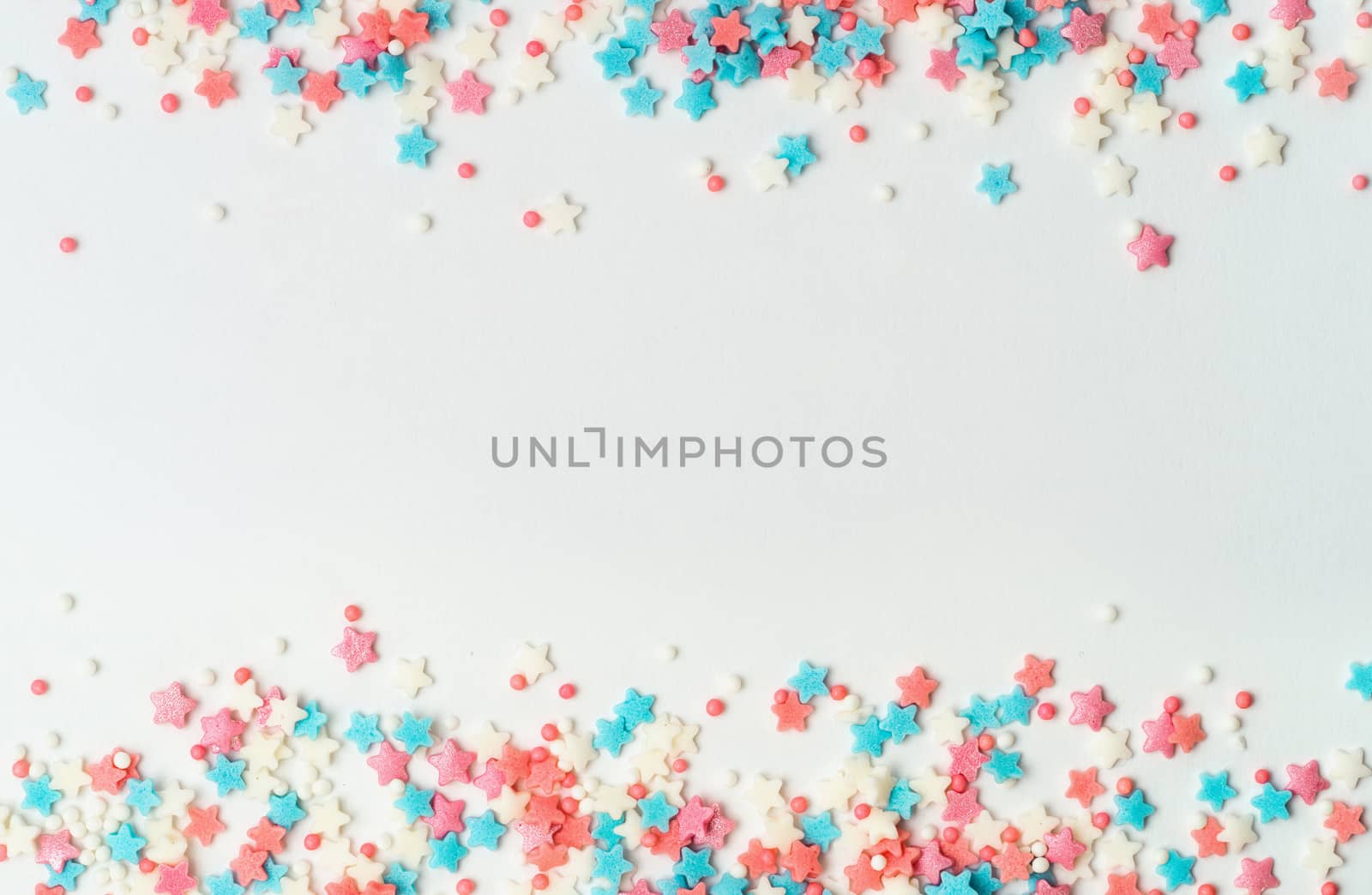 Festive border frame of colorful pastel sprinkles on white background with copy space in center. Sugar sprinkle dots and stars, decoration for cake and bakery. Top view or flat lay. Banner
