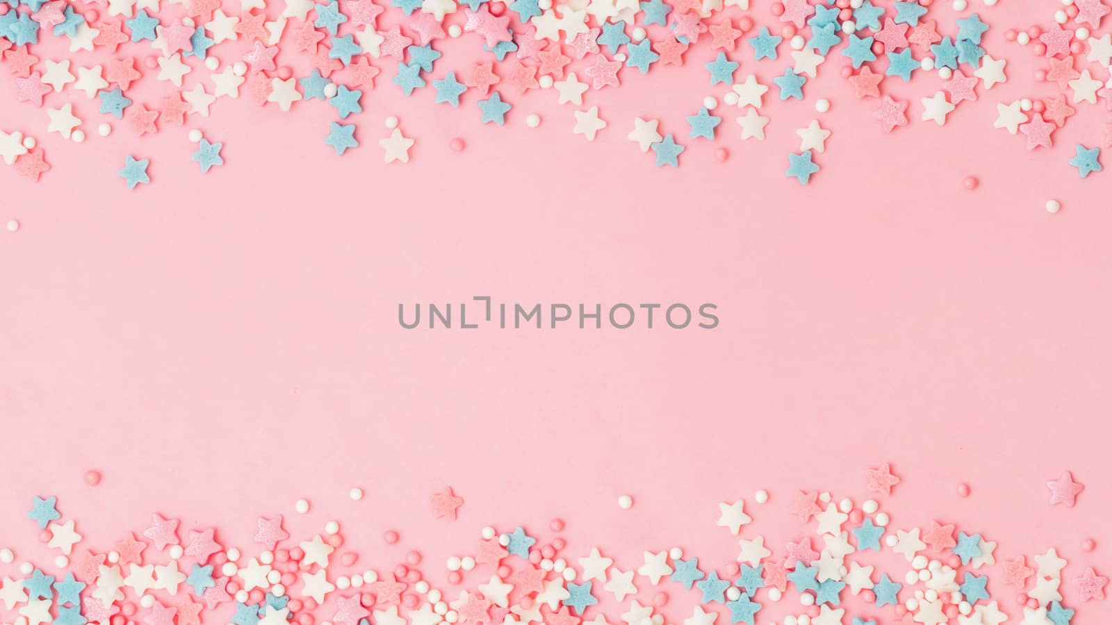 Festive border frame of colorful pastel sprinkles on pink background with copy space in center. Sugar sprinkle dots and stars, decoration for cake and bakery. Top view or flat lay. Banner