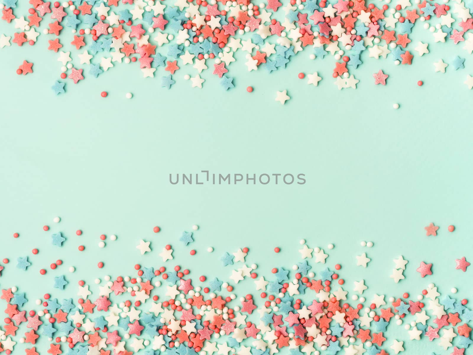 Festive border frame of colorful pastel sprinkles on blue background with copy space in center. Sugar sprinkle dots and stars, decoration for cake and bakery. Top view or flat lay.