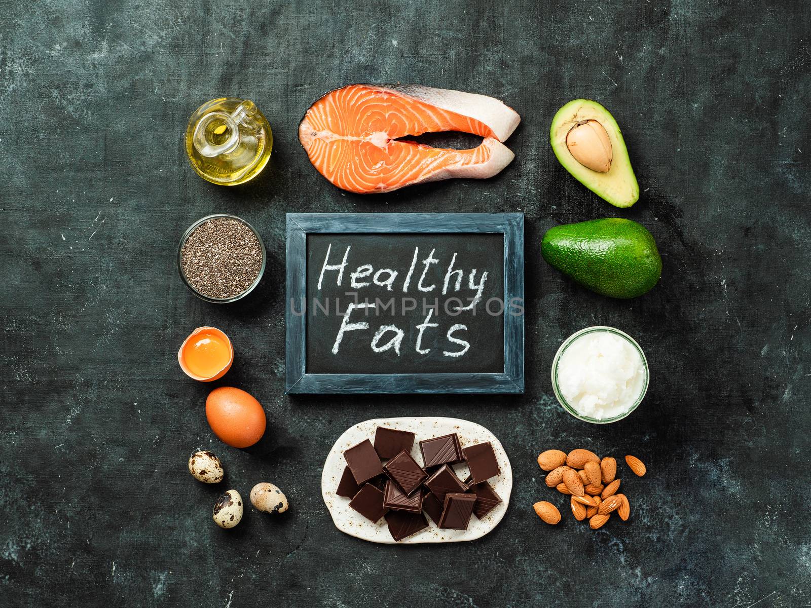 Healthy fats sources concept. Different food ingredients and chalkboard with ealthy Fats words on dark background. Top view or flat lay.