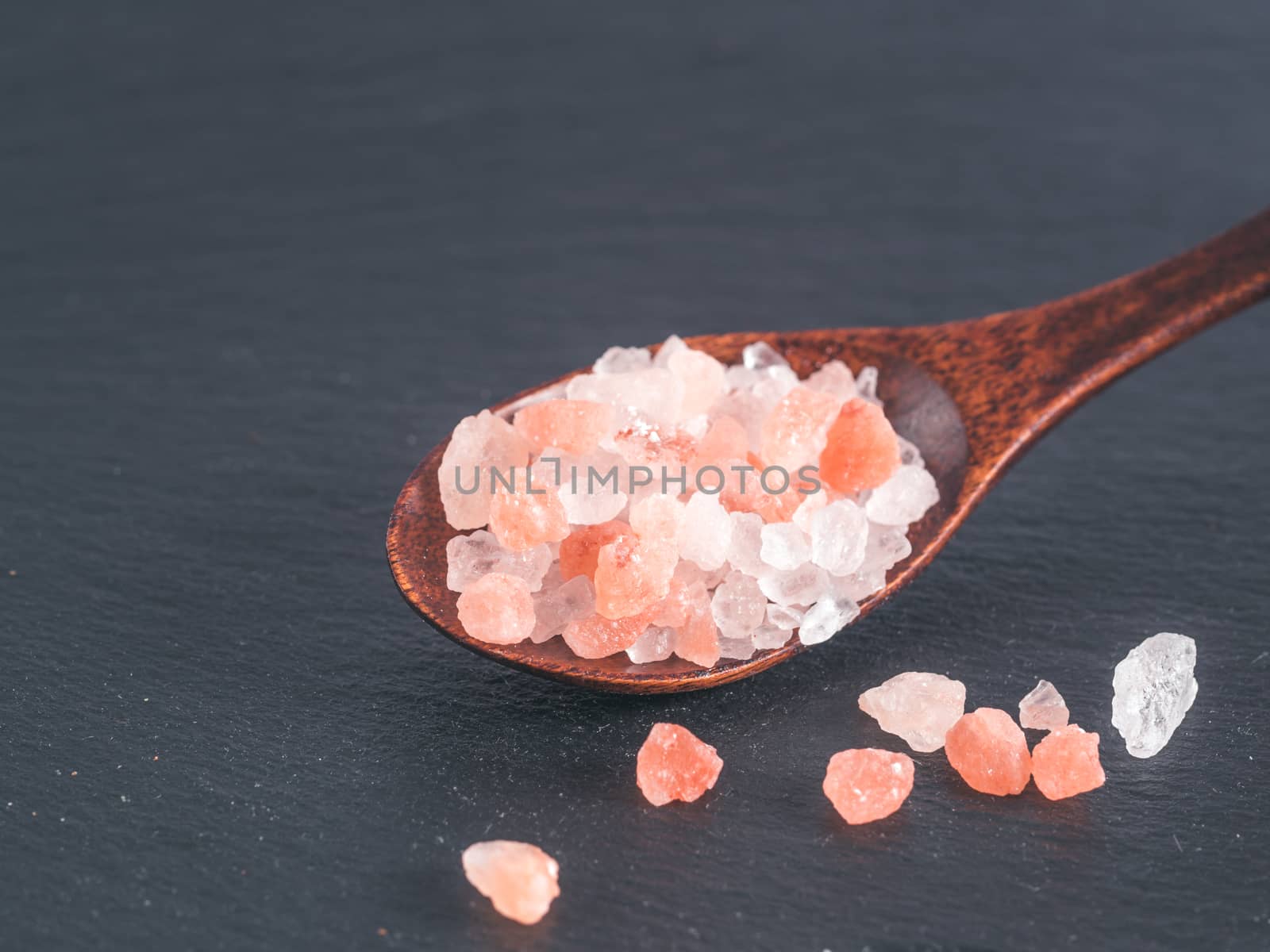 Himalayan pink salt in spoon on black stone background. Copy space
