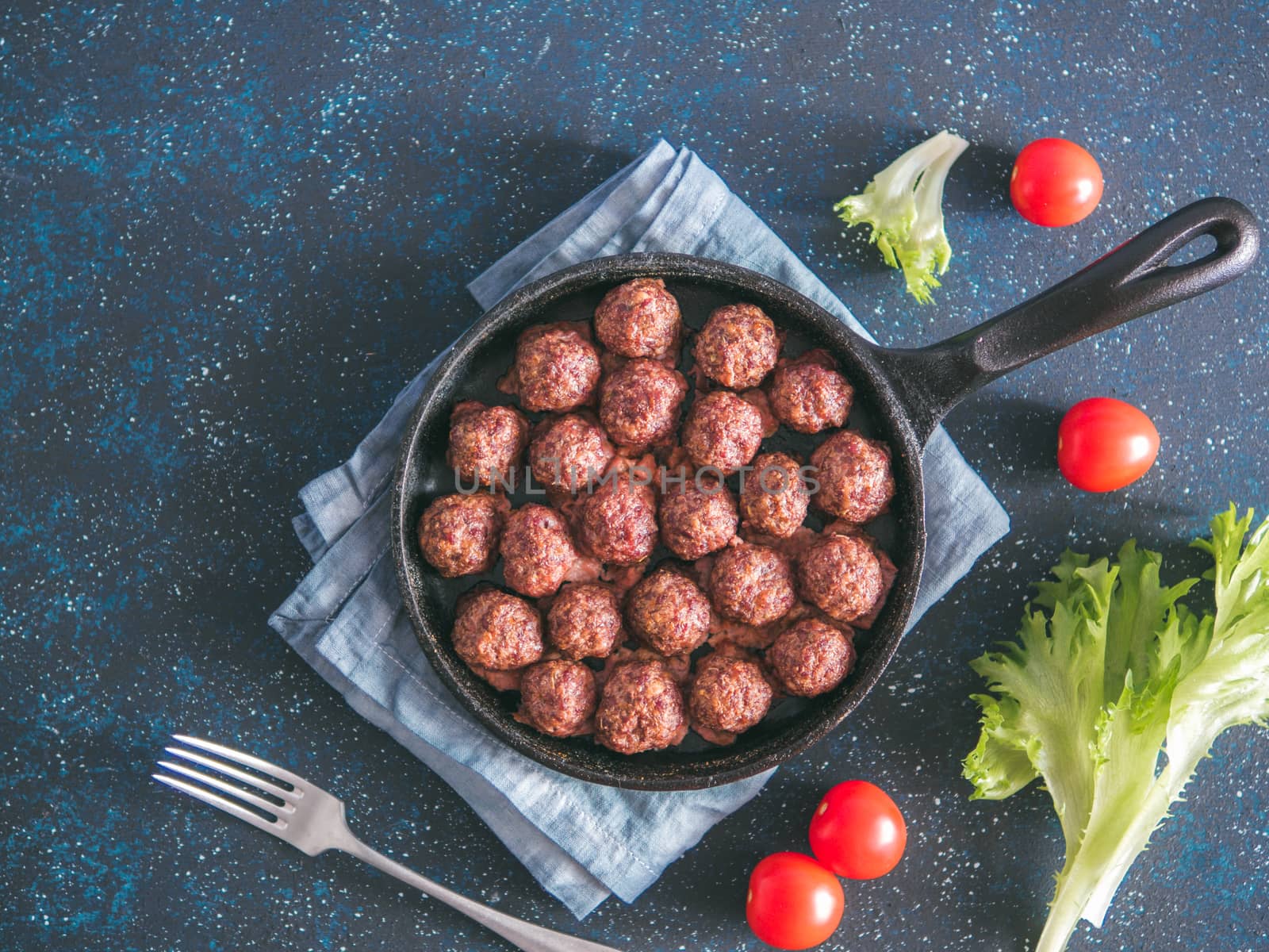Homemade roasted beef meatballs in cast-iron skillet on dark blue background. Top view or flat-lay. Copy space for text.
