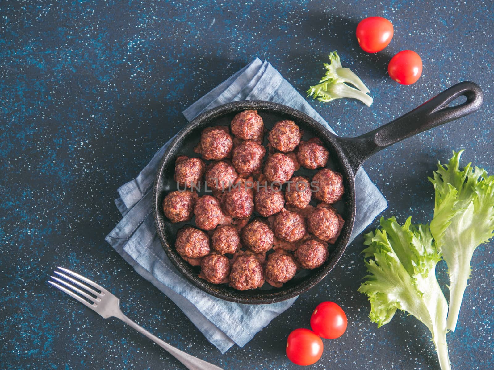 Homemade roasted beef meatballs in cast-iron skillet on dark blue background. Top view or flat-lay. Copy space for text.